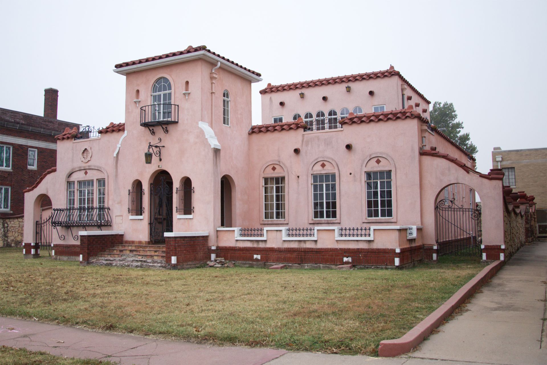 Pink stucco house with arched windows, red tile roof, and a small tower beside a grassy yard