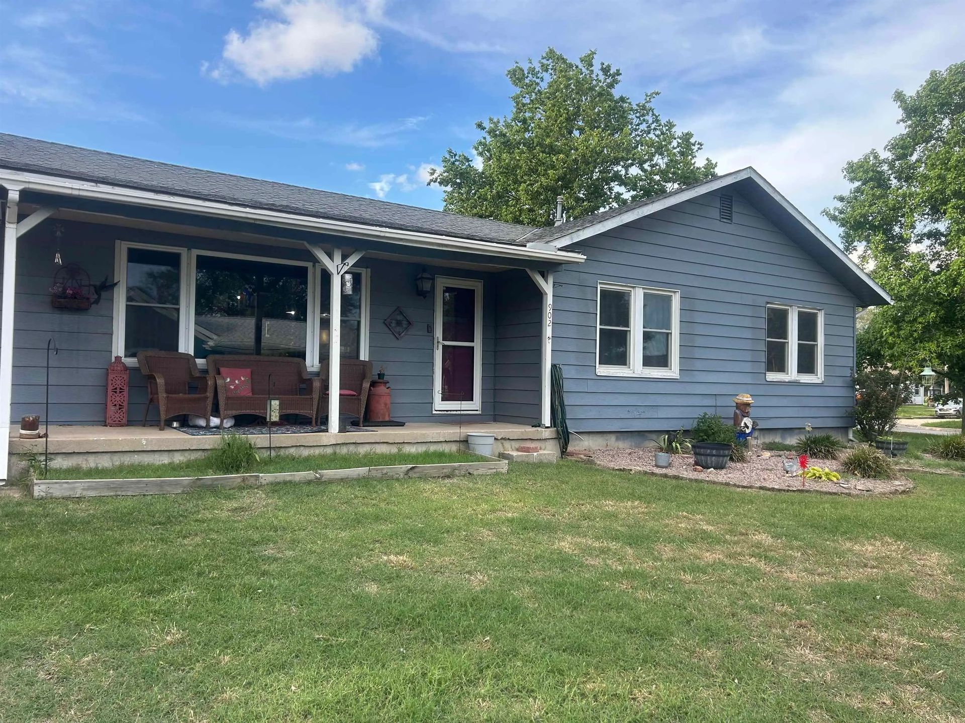 Blue house with a covered porch, front lawn, and flower beds on a sunny day