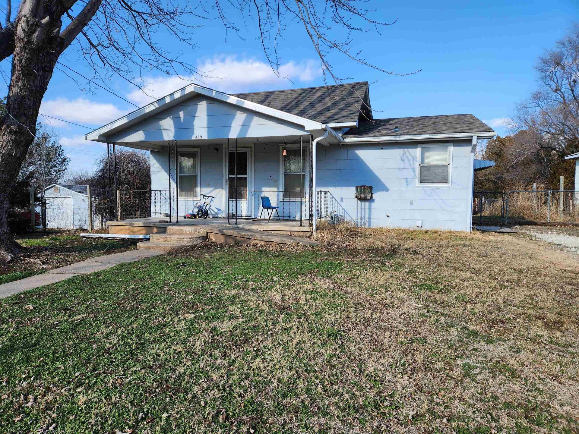 Small light-blue house with a front porch and a bare yard under a clear blue sky