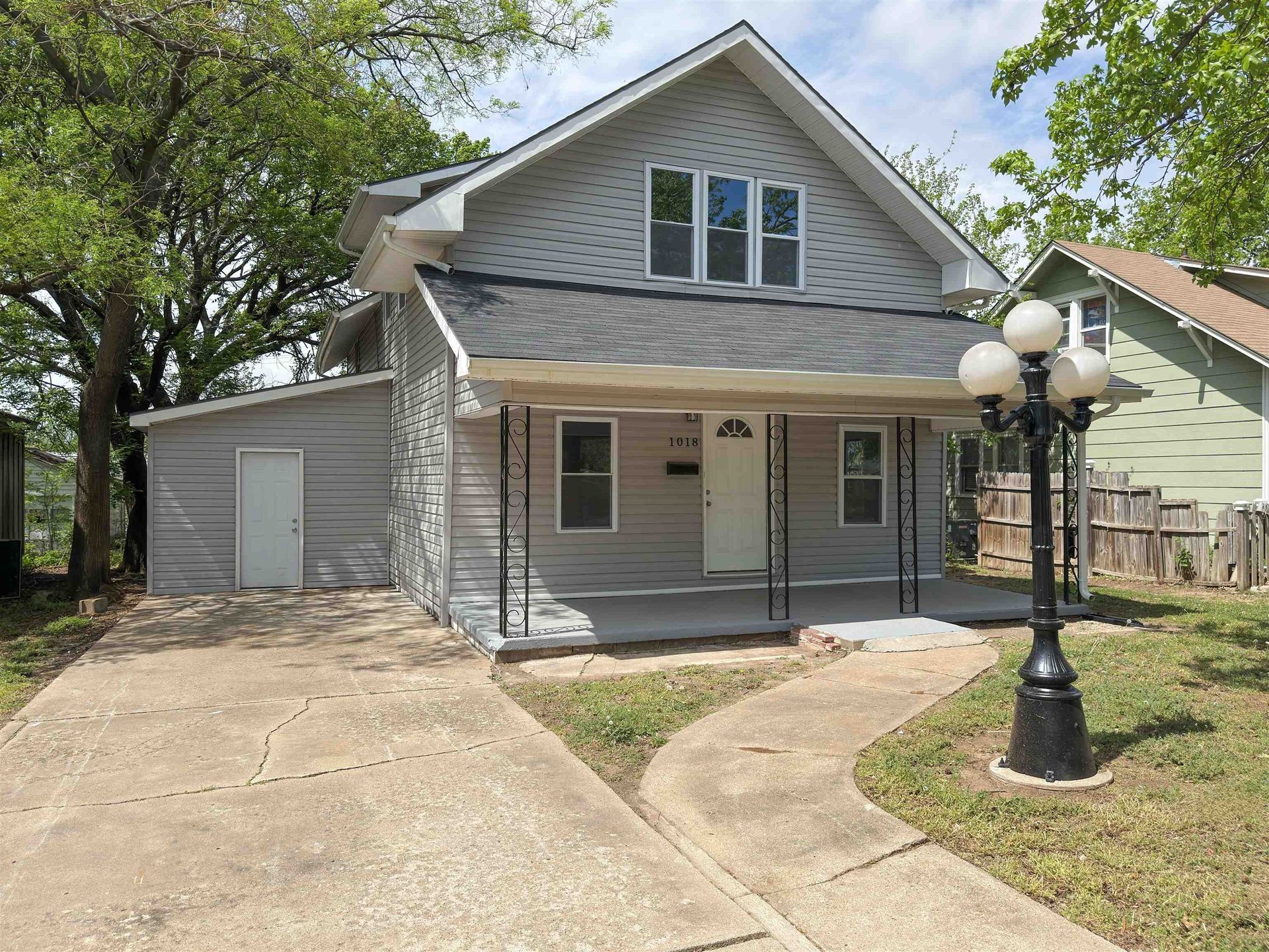 Small gray house with a front porch, driveway, and a lamppost in the yard