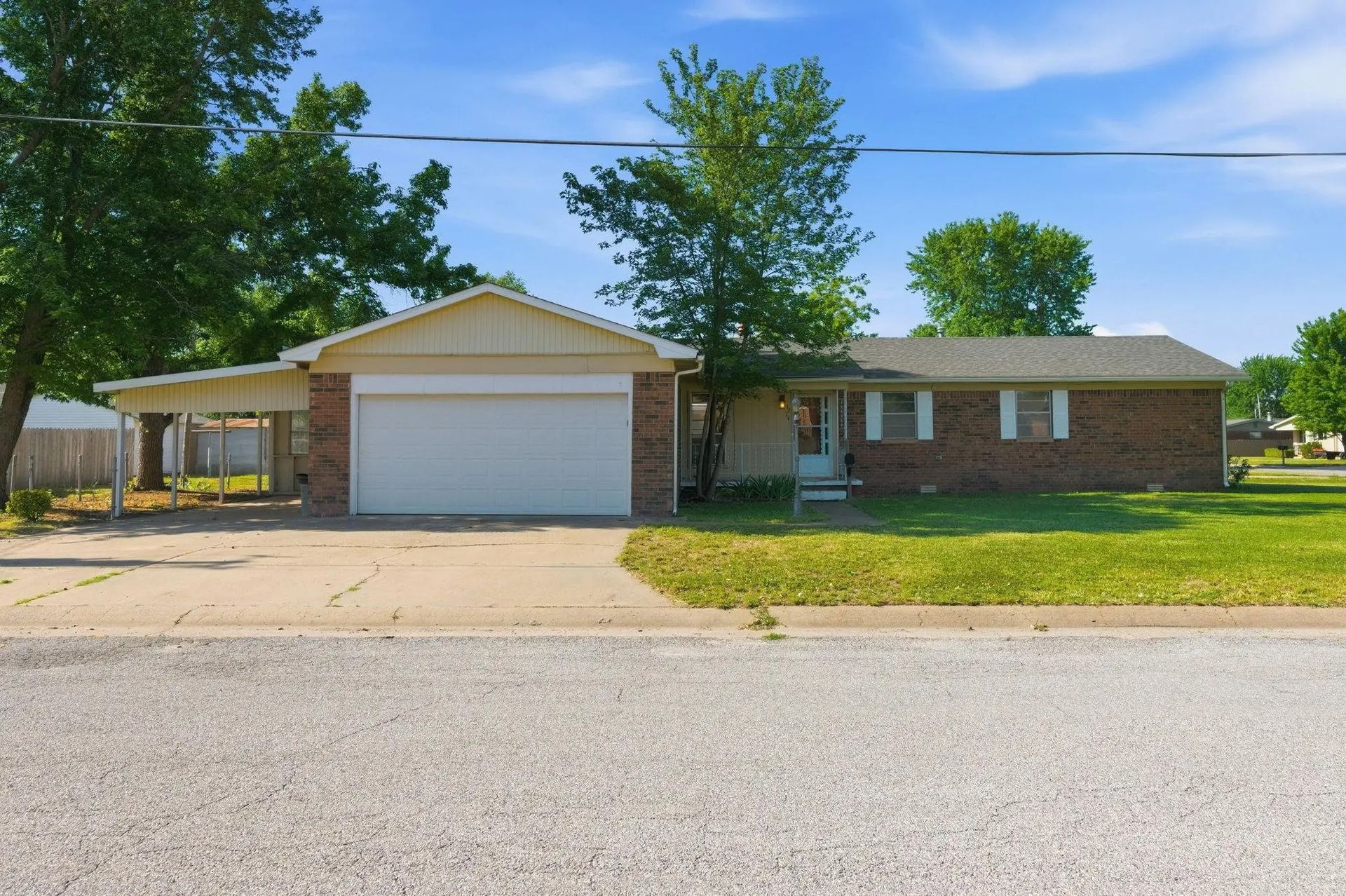 Single-story brick house with white garage and covered carport on a sunny suburban street