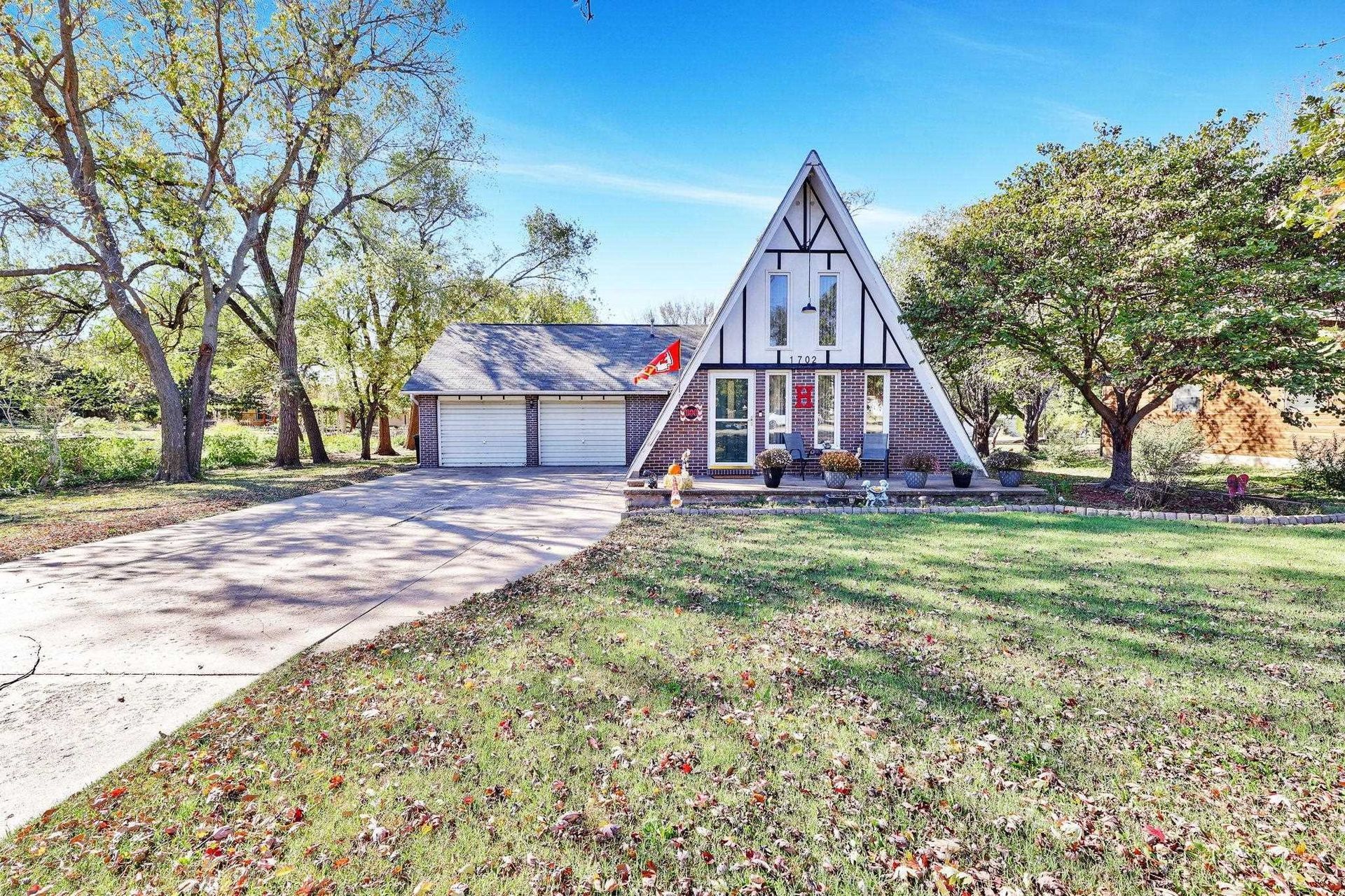 A-frame house with white trim, attached garage, and a tree-lined front lawn under bright daylight