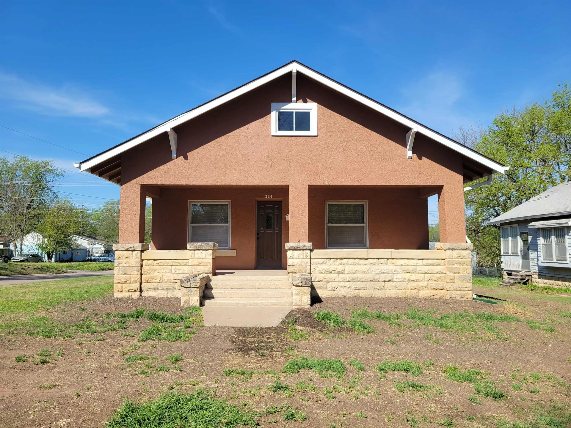 Small brick house with a front porch, stone base, and central steps under a clear blue sky.
