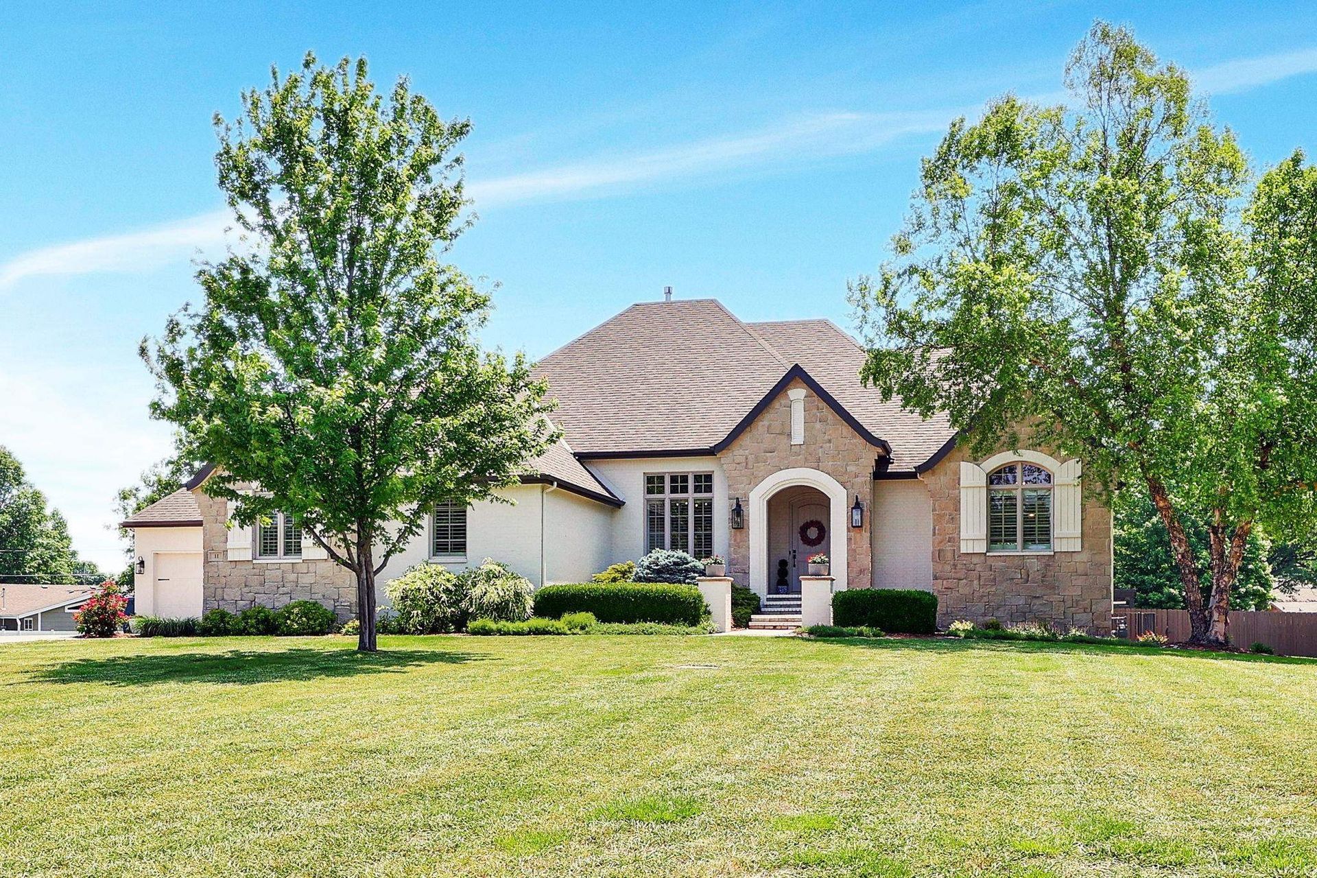 Suburban brick house with a manicured lawn and trees under a blue sky