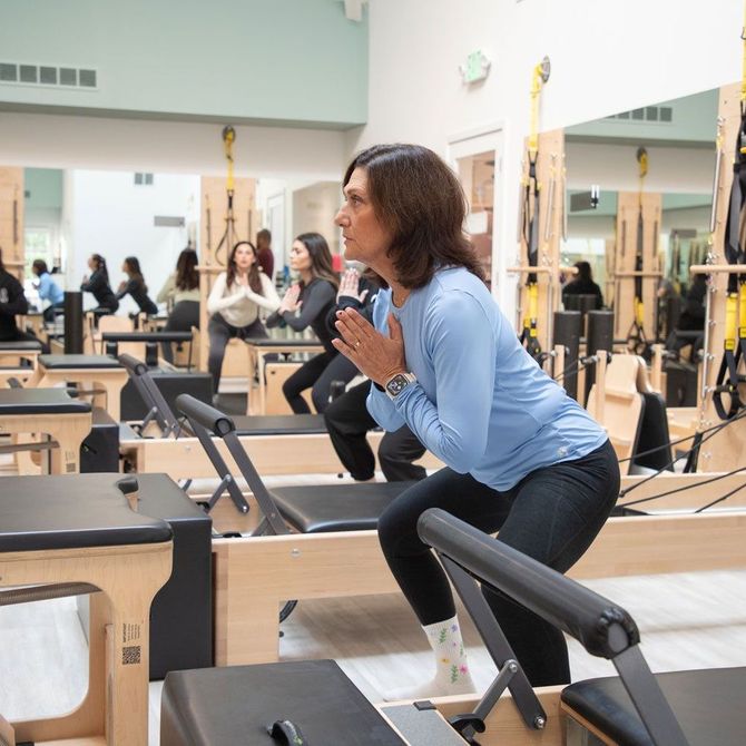 A woman is squatting on a pilates machine in a gym