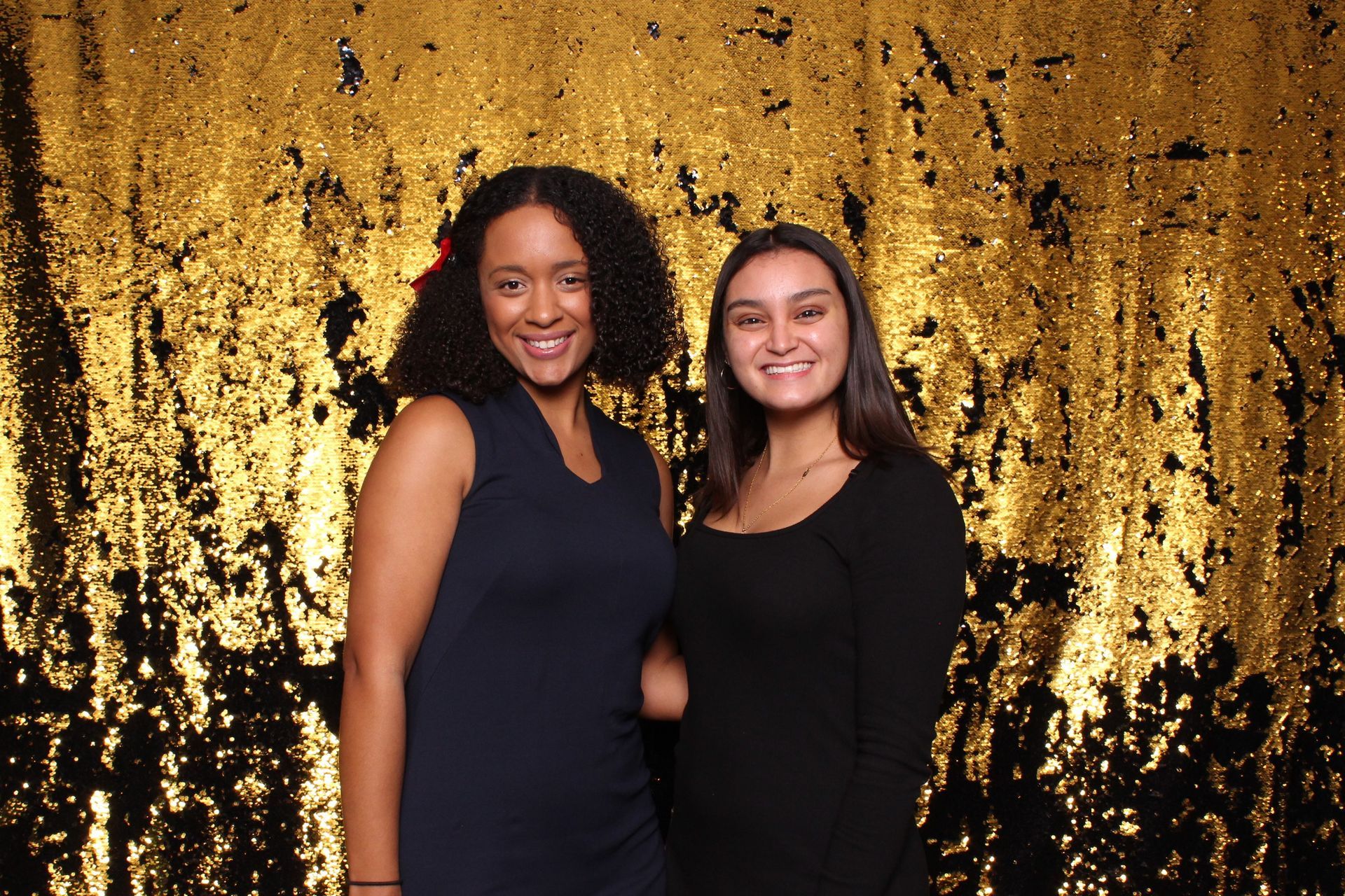 two women are posing for a picture in front of a gold sequined backdrop .