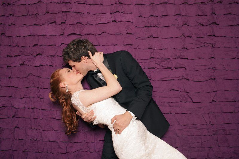 A bride and groom are kissing in front of a purple wall.