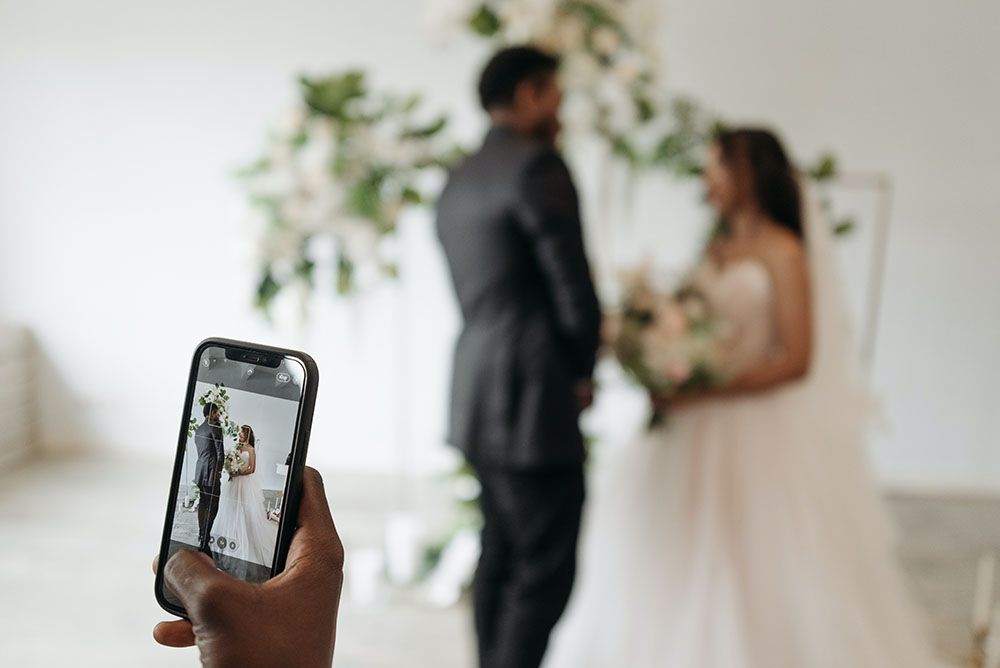 A wedding content creator is taking a picture of a bride and groom on their wedding day.