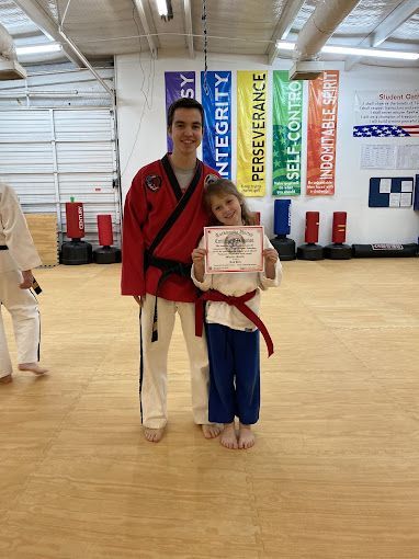 A man and a girl are standing next to each other in a karate dojo holding a certificate.