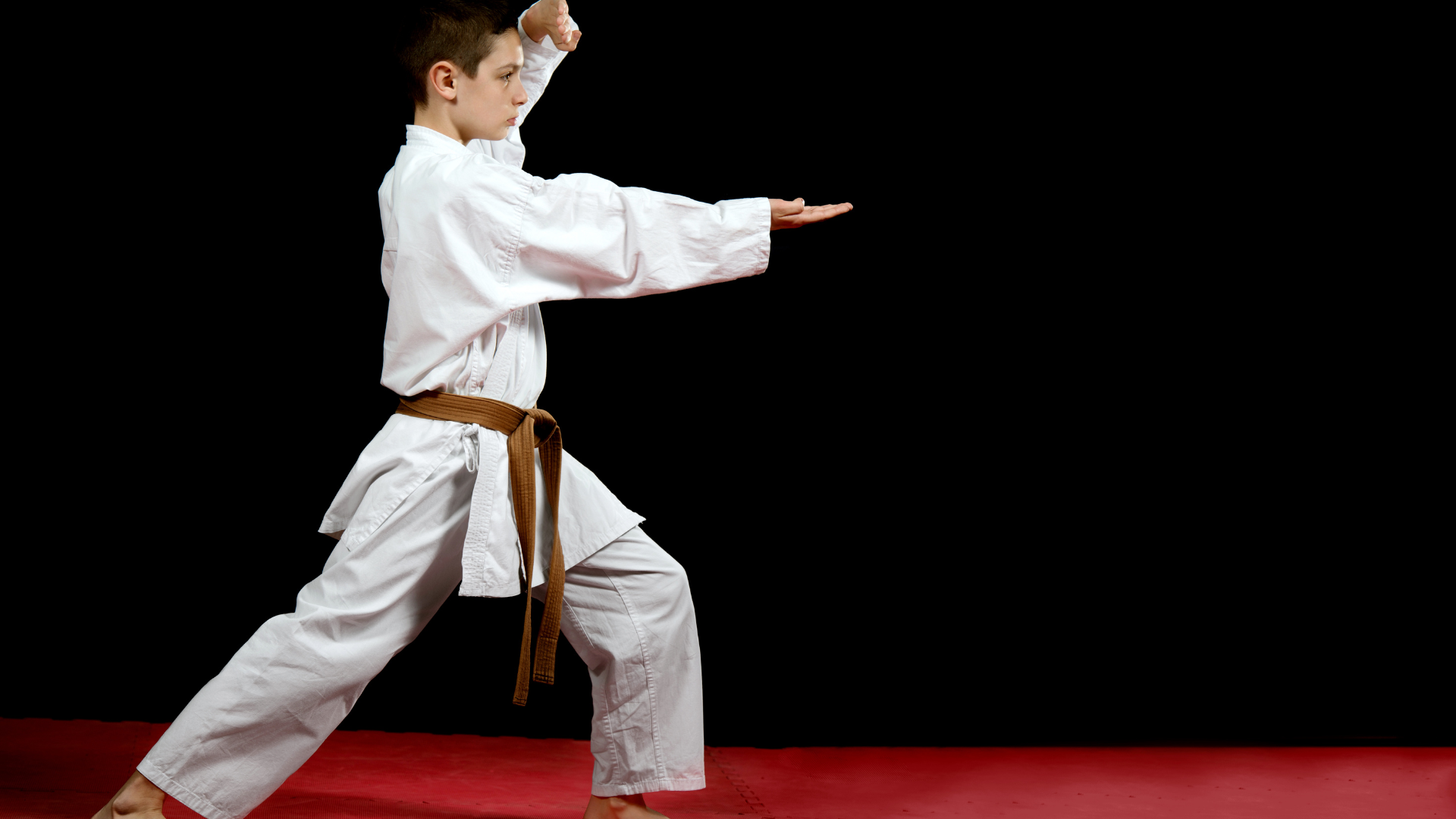A young boy is practicing karate on a red mat.