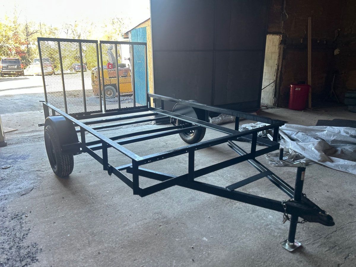 Black utility trailer with mesh front, parked on concrete.