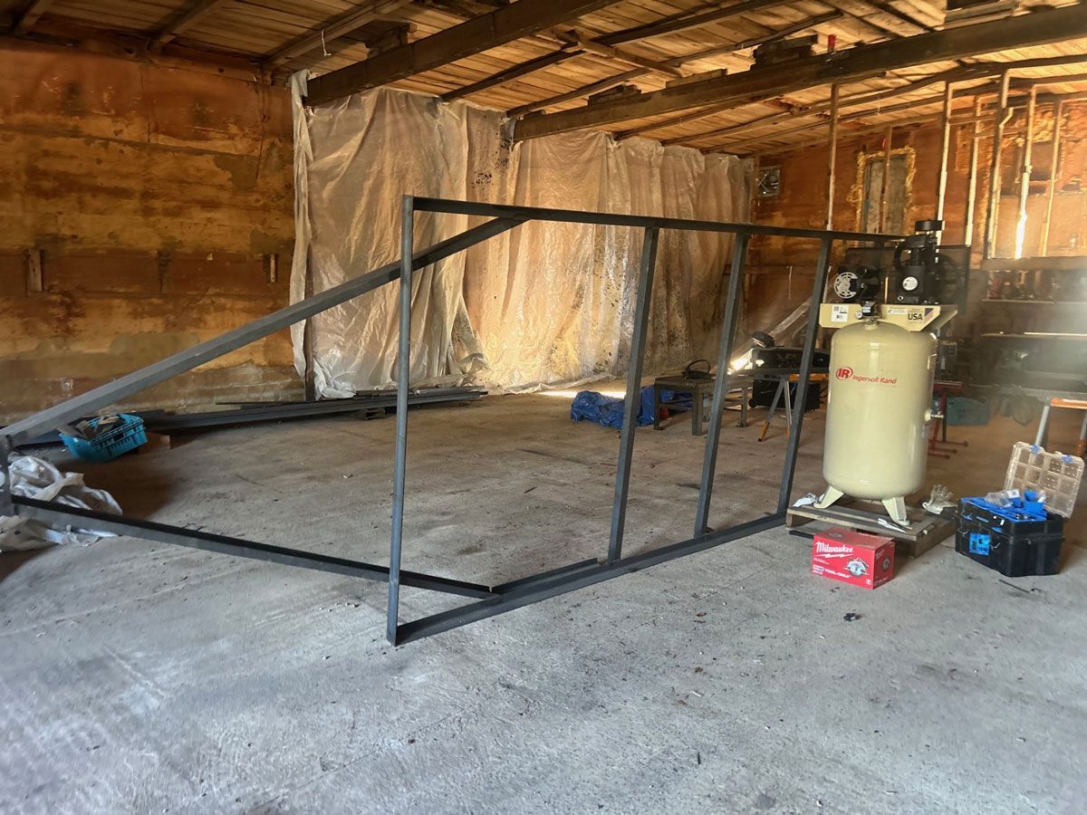 Metal frame construction inside a dusty, unfinished building with an air compressor.
