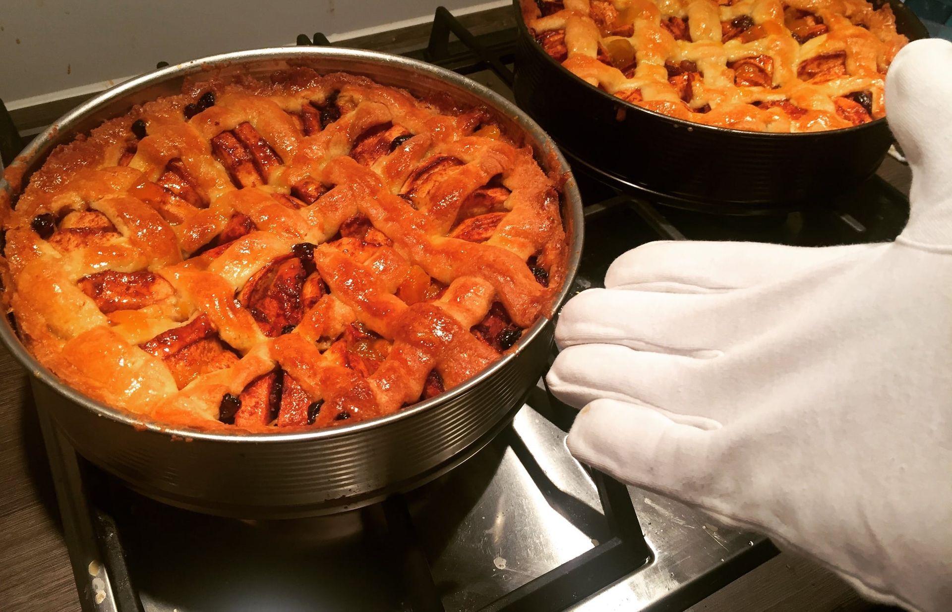 Een persoon met witte handschoenen houdt een pan met taart vast op het fornuis.