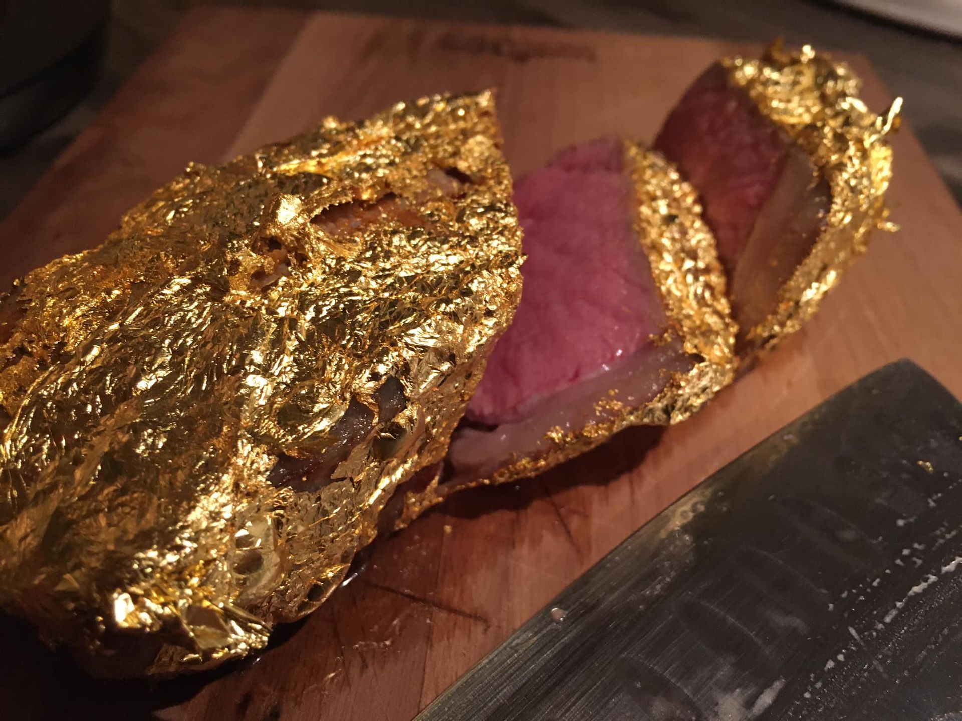 Een stuk vlees verpakt in goudfolie op een snijplank