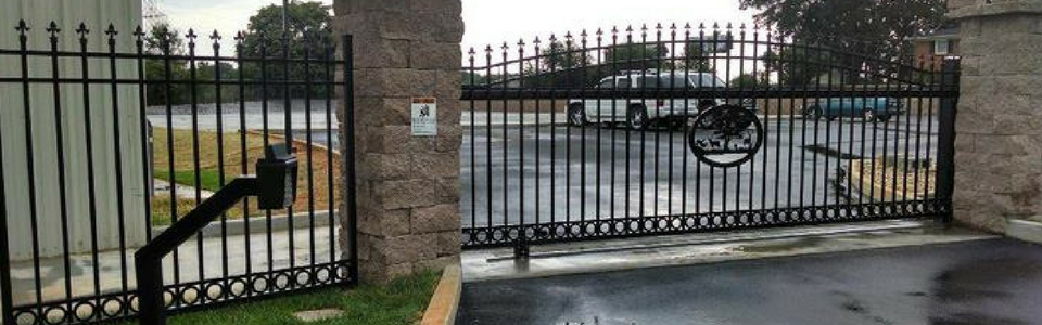 A black wrought iron gate is open to a parking lot.