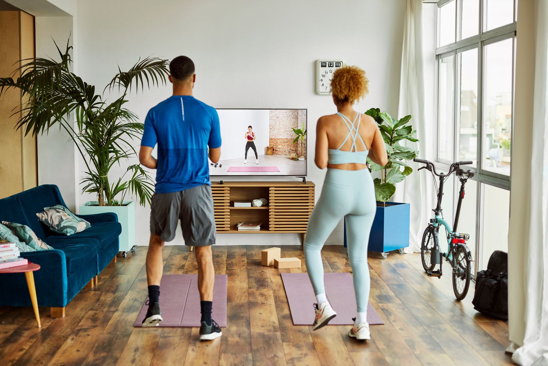 A man and a woman are standing on yoga mats in front of a television in a living room.