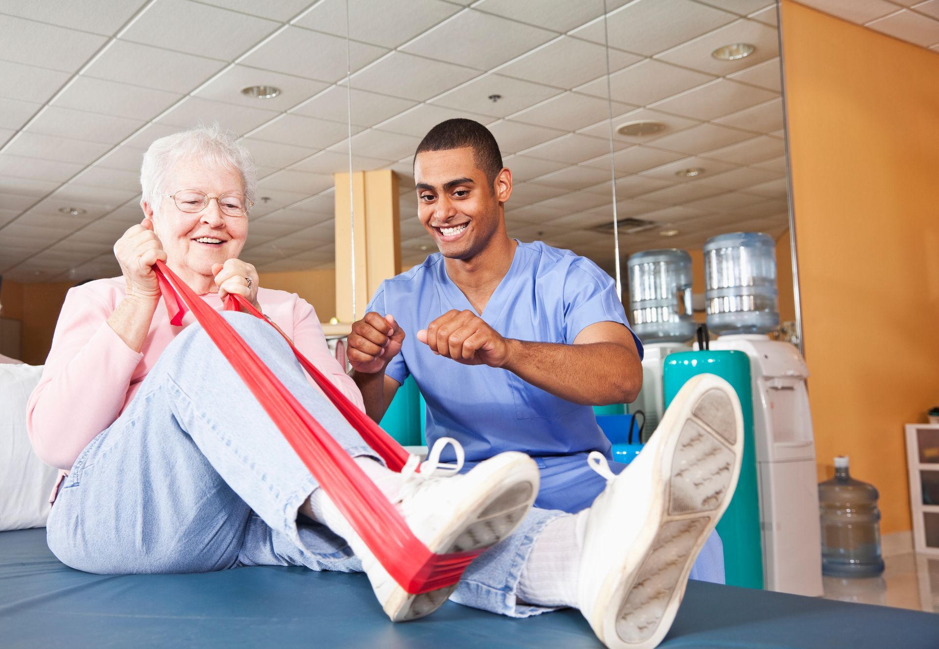 A man is helping an elderly woman do exercises with a resistance band.