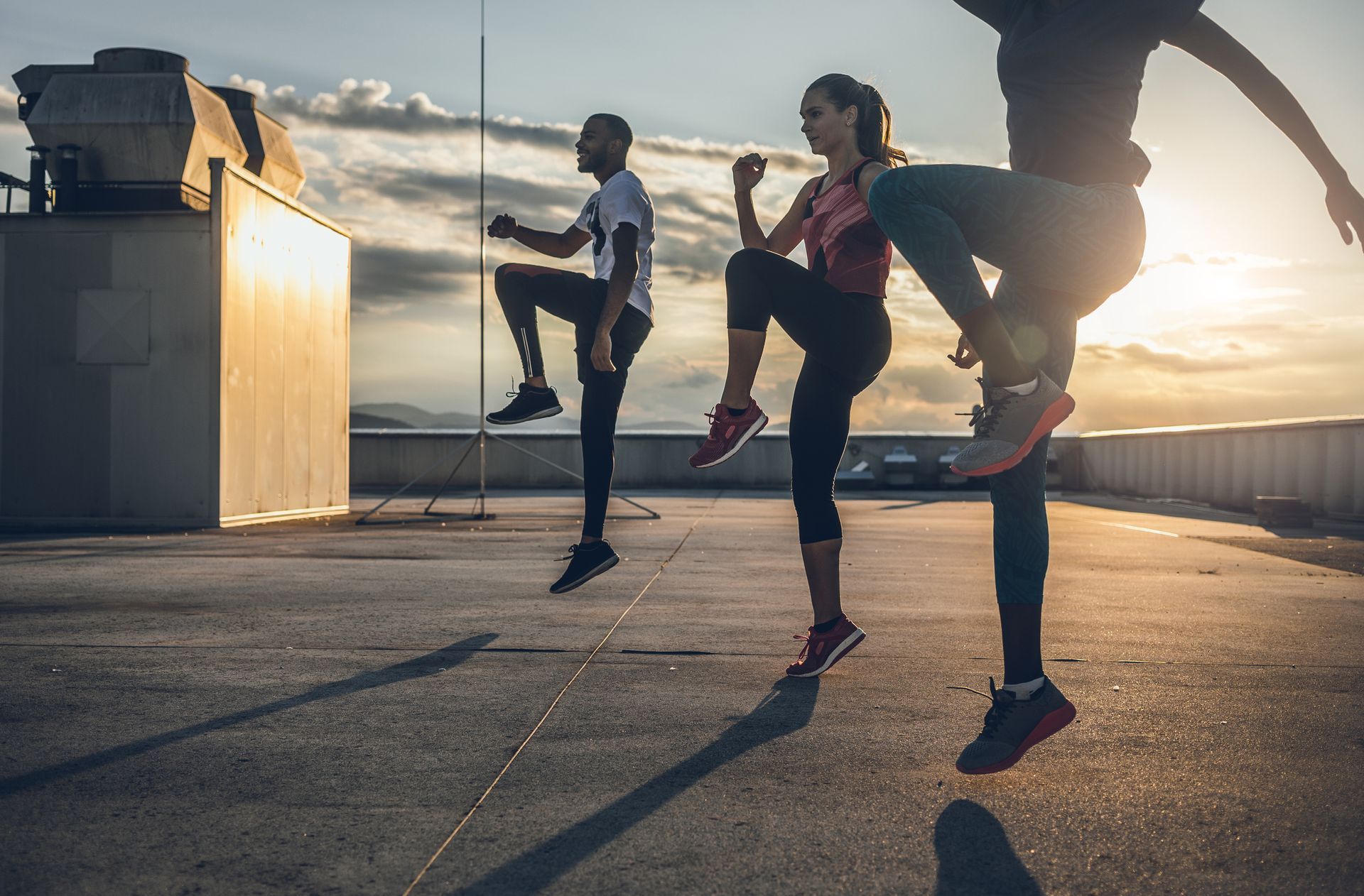 A group of people are doing exercises on a rooftop at sunset.