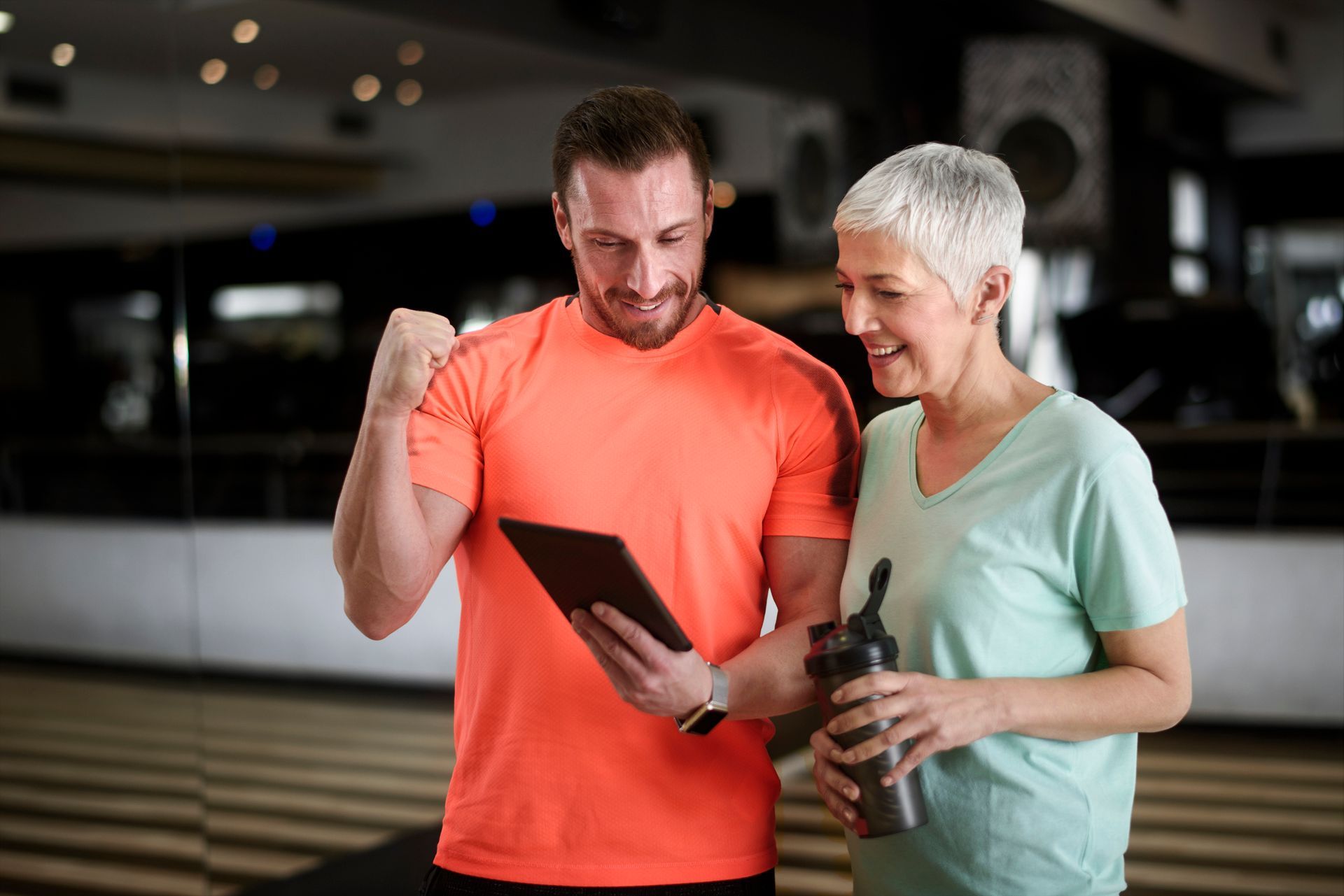 A man and a woman are looking at a tablet in a gym.