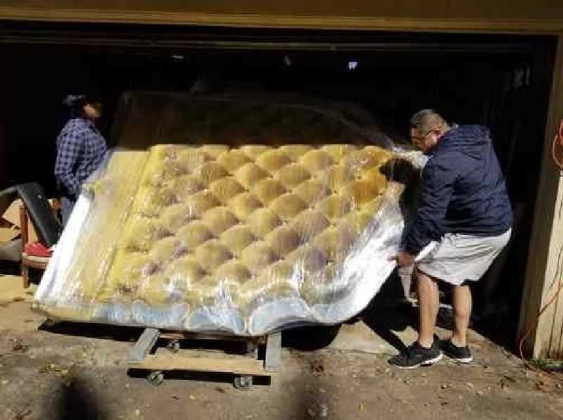Two men are carrying a large mattress into a garage.