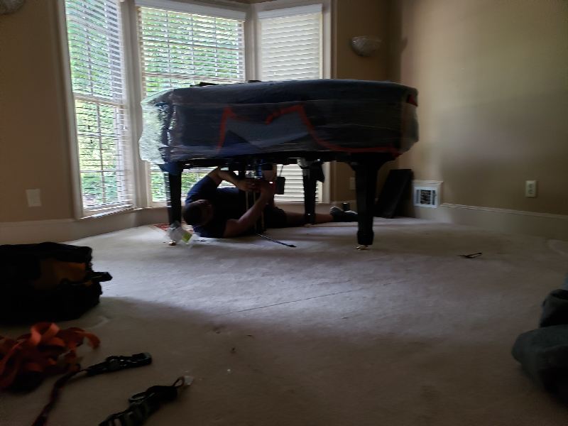 A man is laying under a piano in a living room.