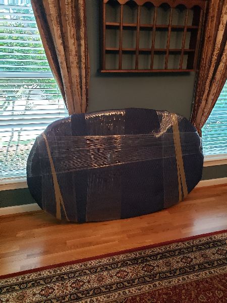 A couch is wrapped in plastic wrap in a living room next to a window.