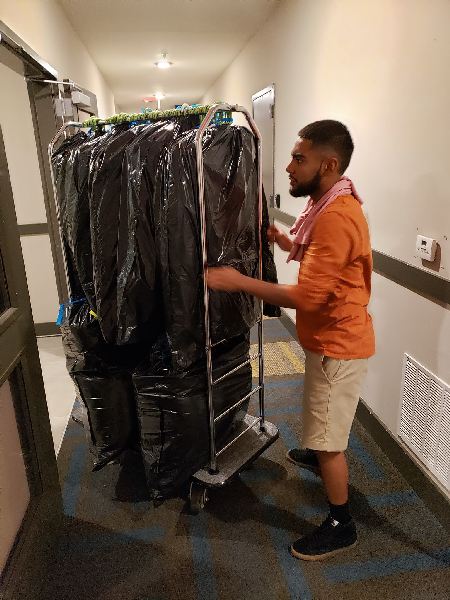 A man is carrying a cart filled with clothes in a hallway.