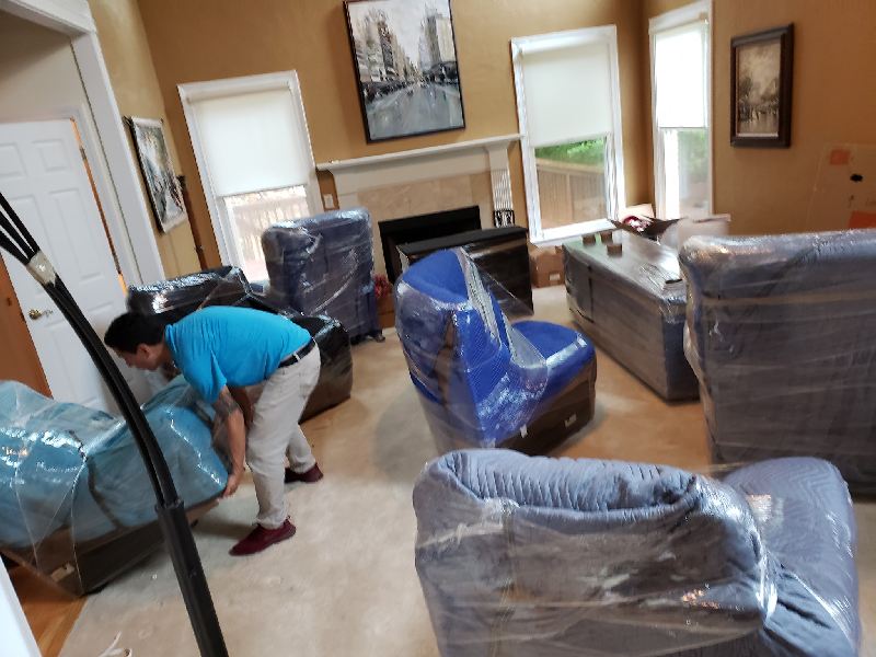 A man is moving furniture in a living room covered in plastic wrap.