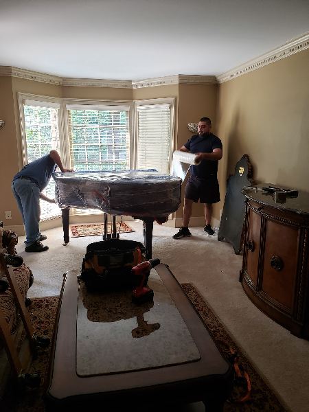 Two men are moving a piano in a living room.