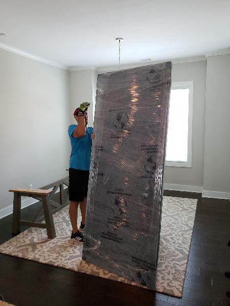 A man is holding a large piece of wrapped plastic in a room.