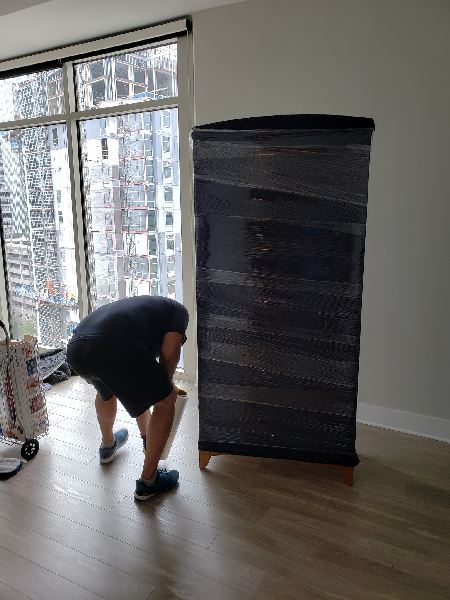 A man is wrapping a dresser in plastic wrap in a living room.