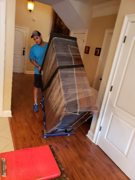 A man is pushing a large box on a dolly in a hallway