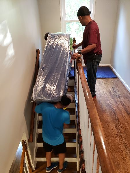 Two men are carrying a mattress up a set of stairs.