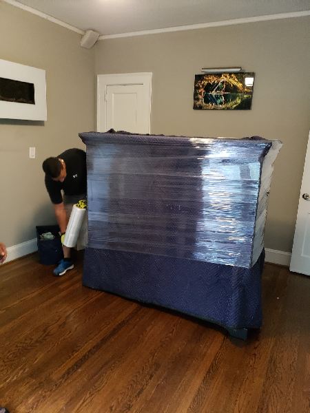 A man is wrapping a piano in plastic wrap in a living room.