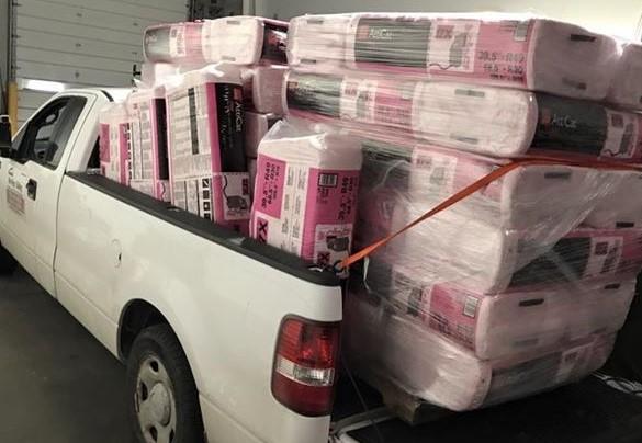 A white truck is loaded with pink boxes in the back.