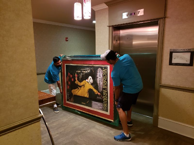 Two men are carrying a large framed picture into an elevator.