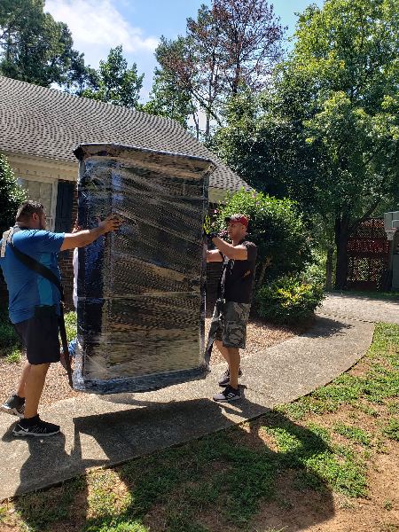Two men are carrying a large refrigerator in front of a house.