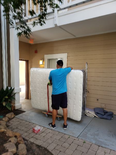 A man in a blue shirt is pushing a mattress on a cart