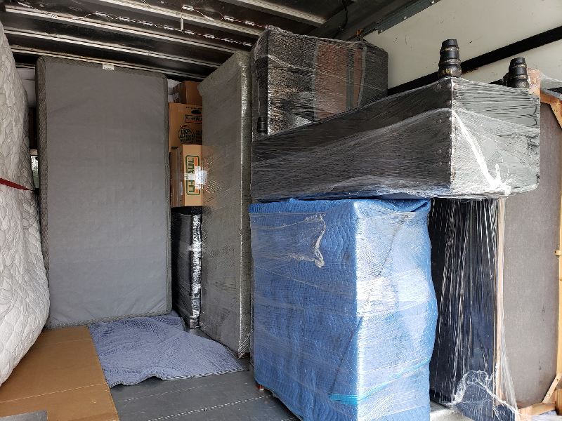 A moving truck filled with lots of furniture wrapped in plastic.