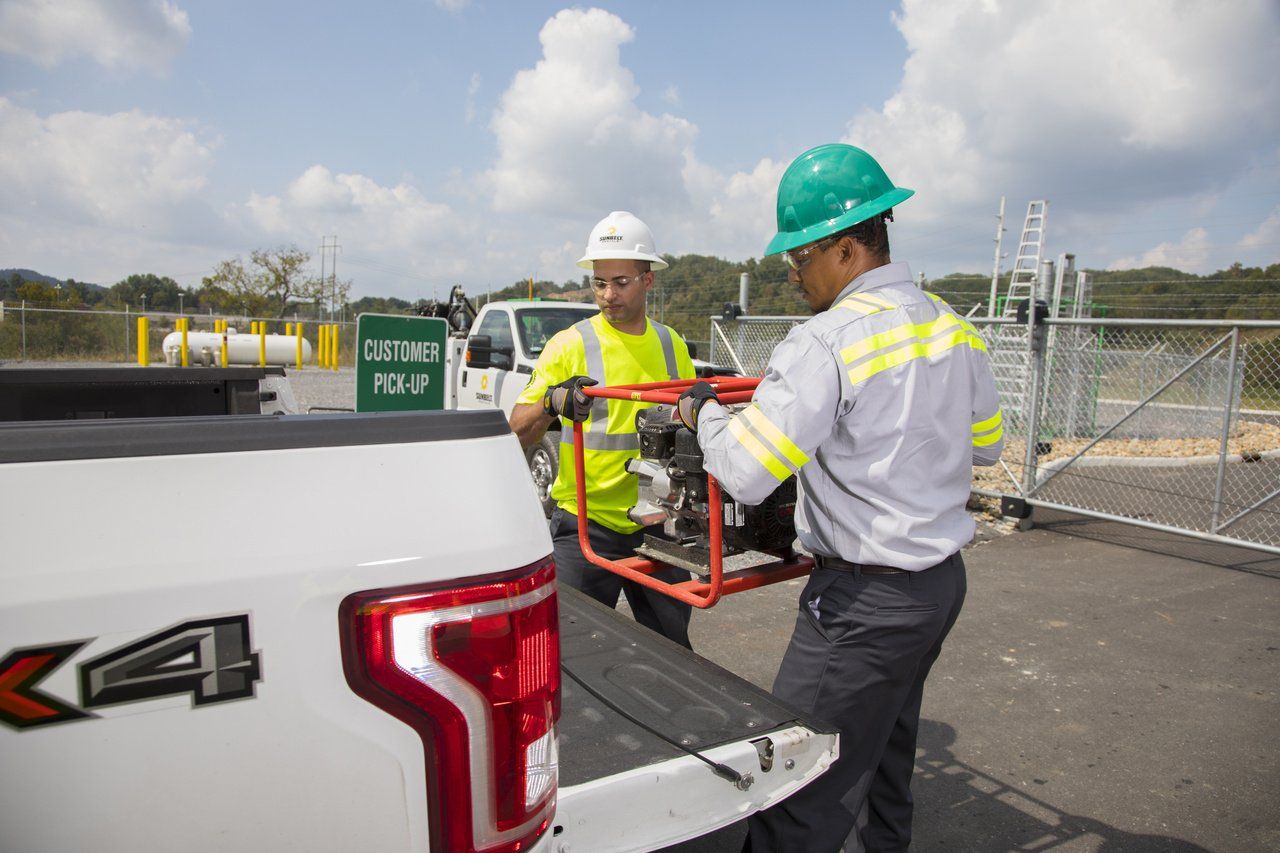 Two men are loading a tool into the back of a truck.