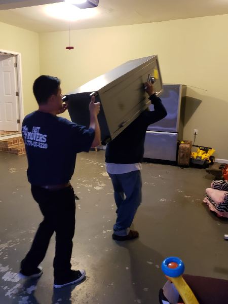 Two men are carrying a large safe in a garage.