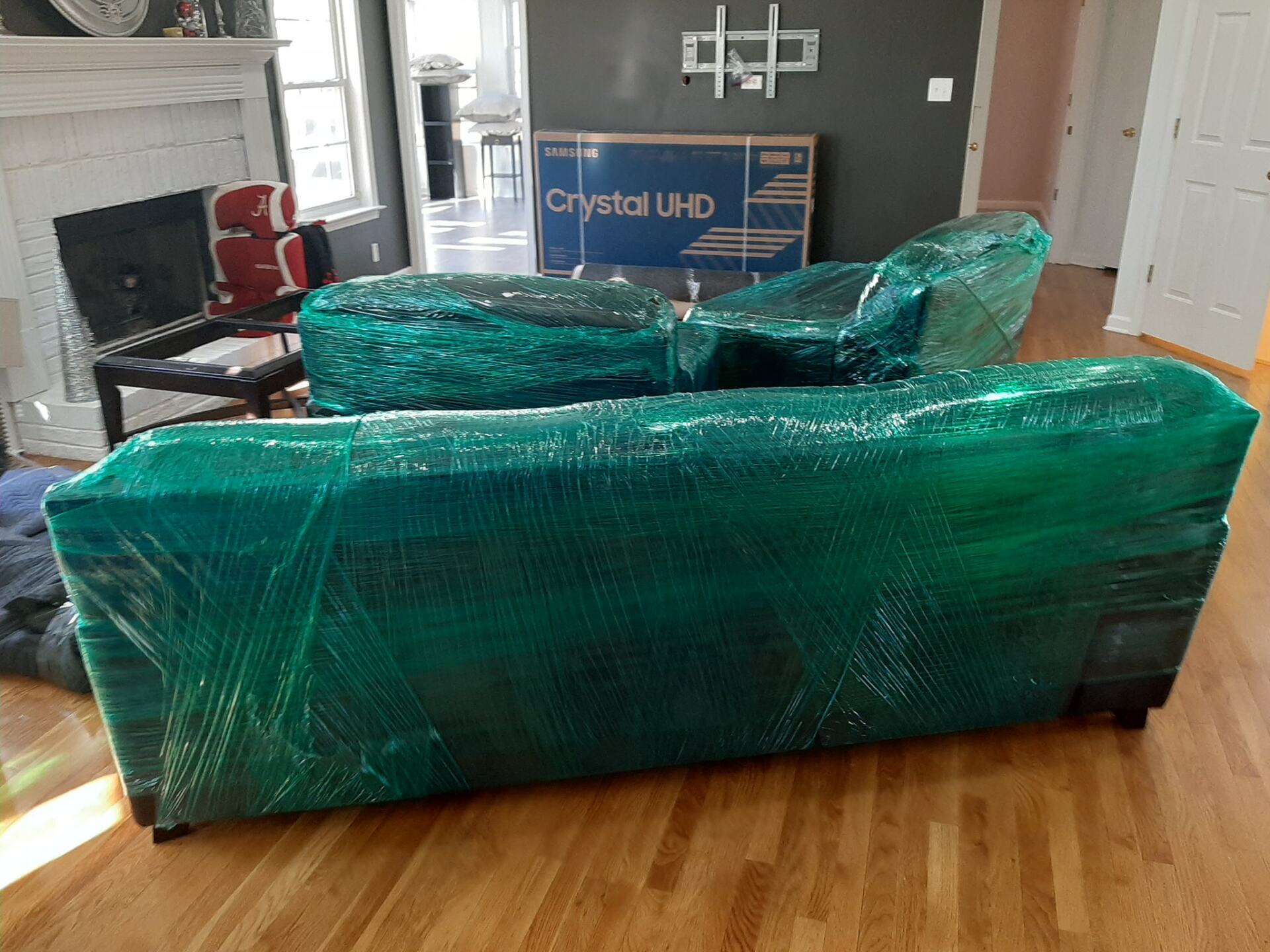 A couch is wrapped in green plastic in a living room.