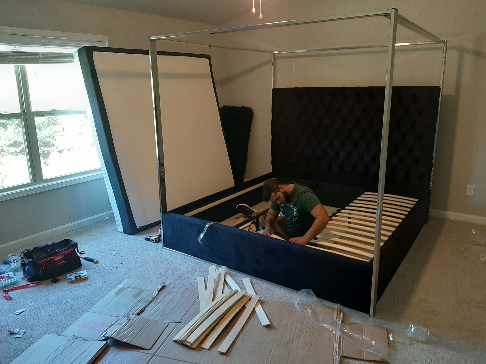 A man is working on a canopy bed in a bedroom.