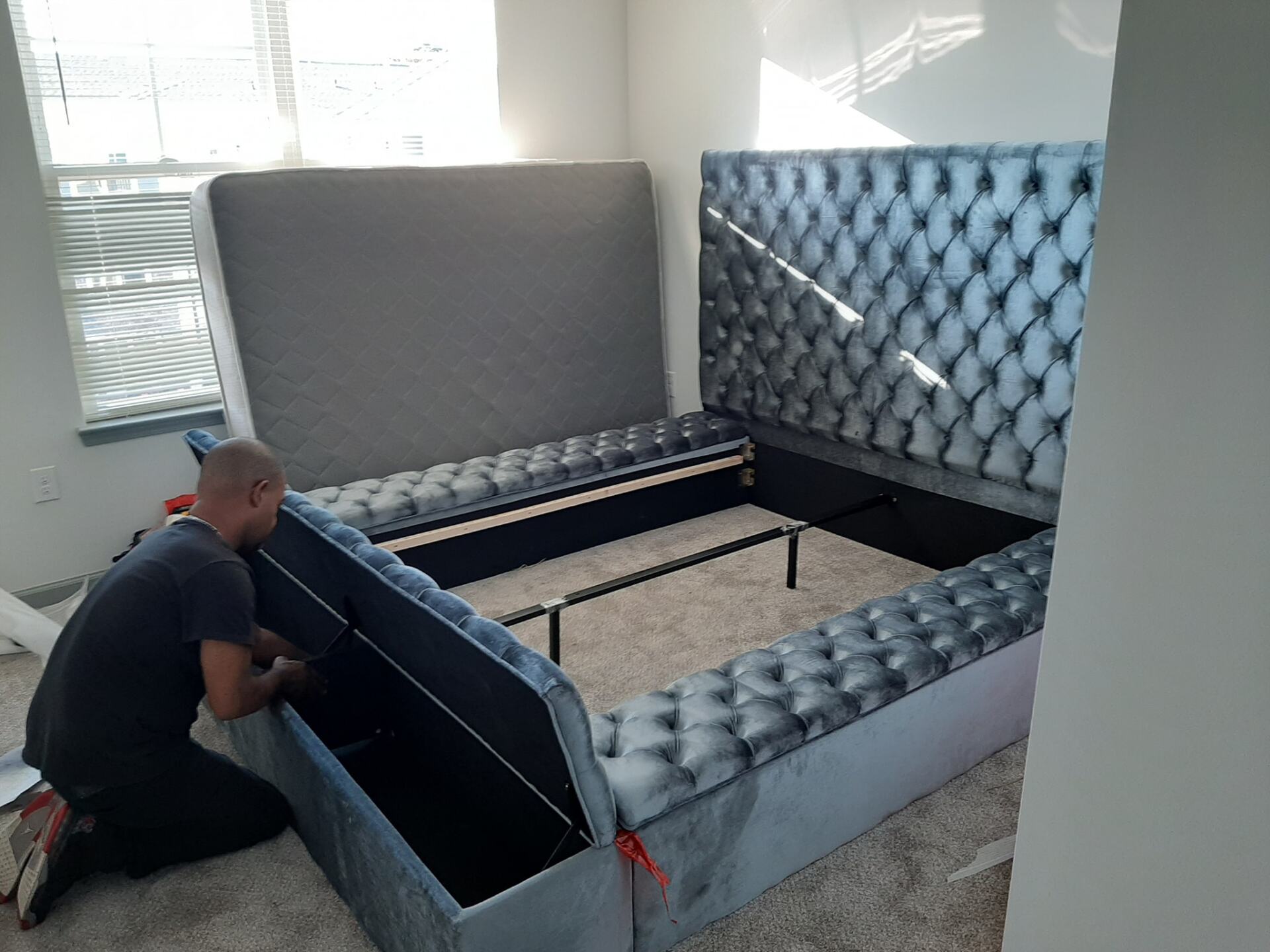 A man is kneeling down next to a bed in a bedroom.