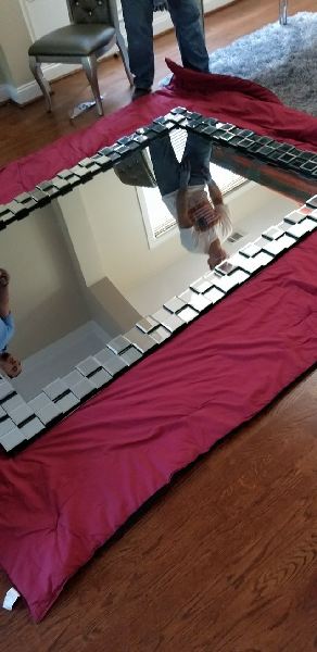 A large mirror is sitting on top of a red blanket on a wooden floor.