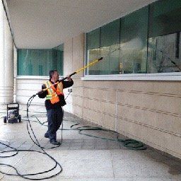 A man is cleaning a building with a high pressure washer.