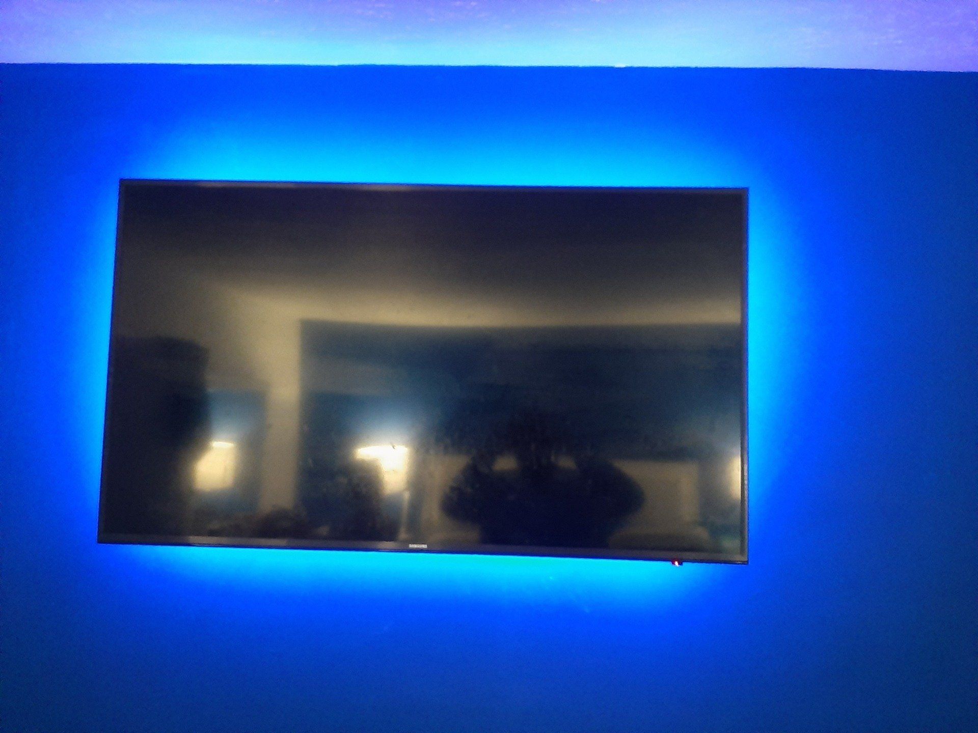 A flat screen tv is hanging on a blue wall with blue lights around it.