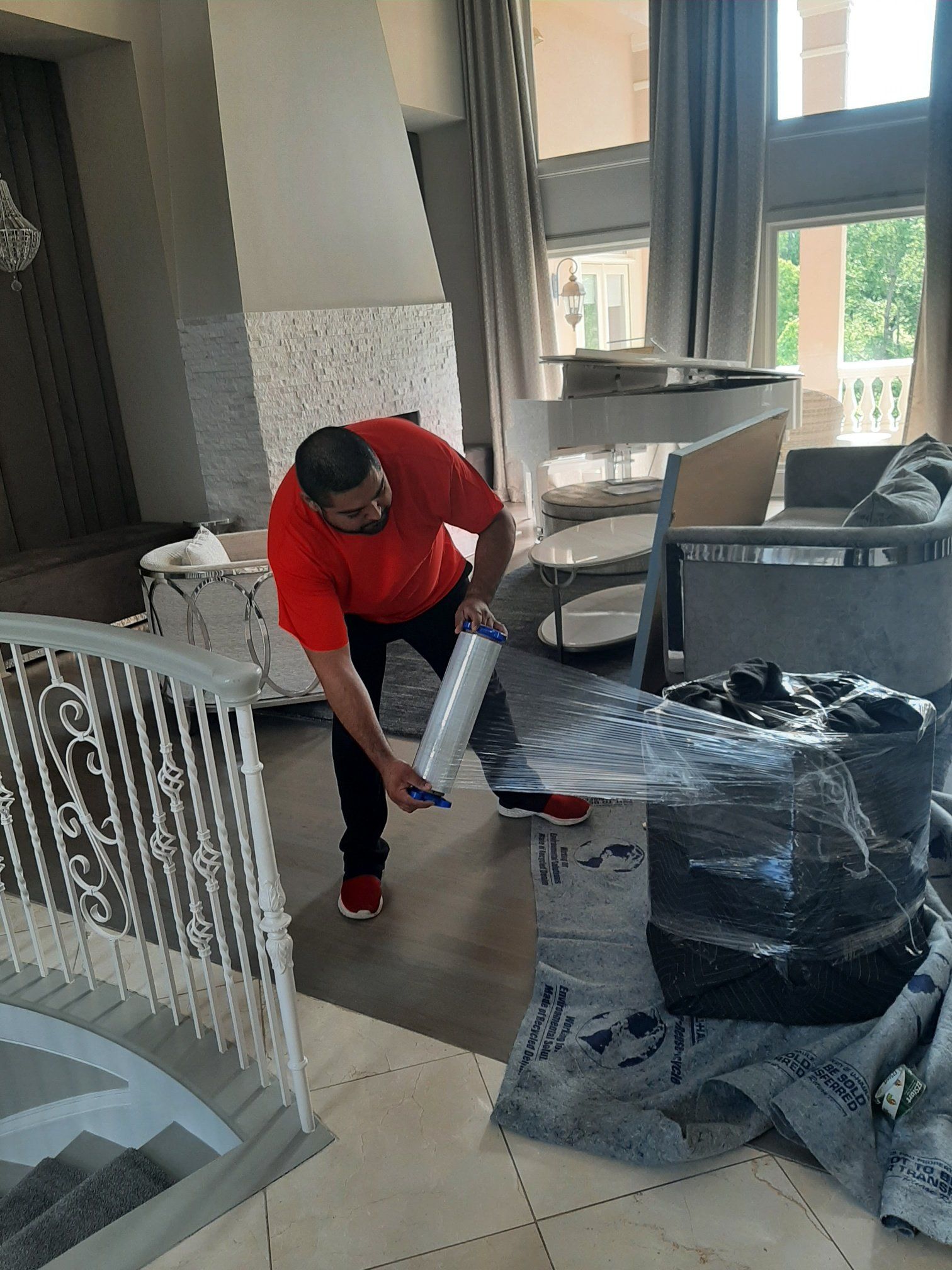 A man is wrapping a chair in plastic wrap in a living room.