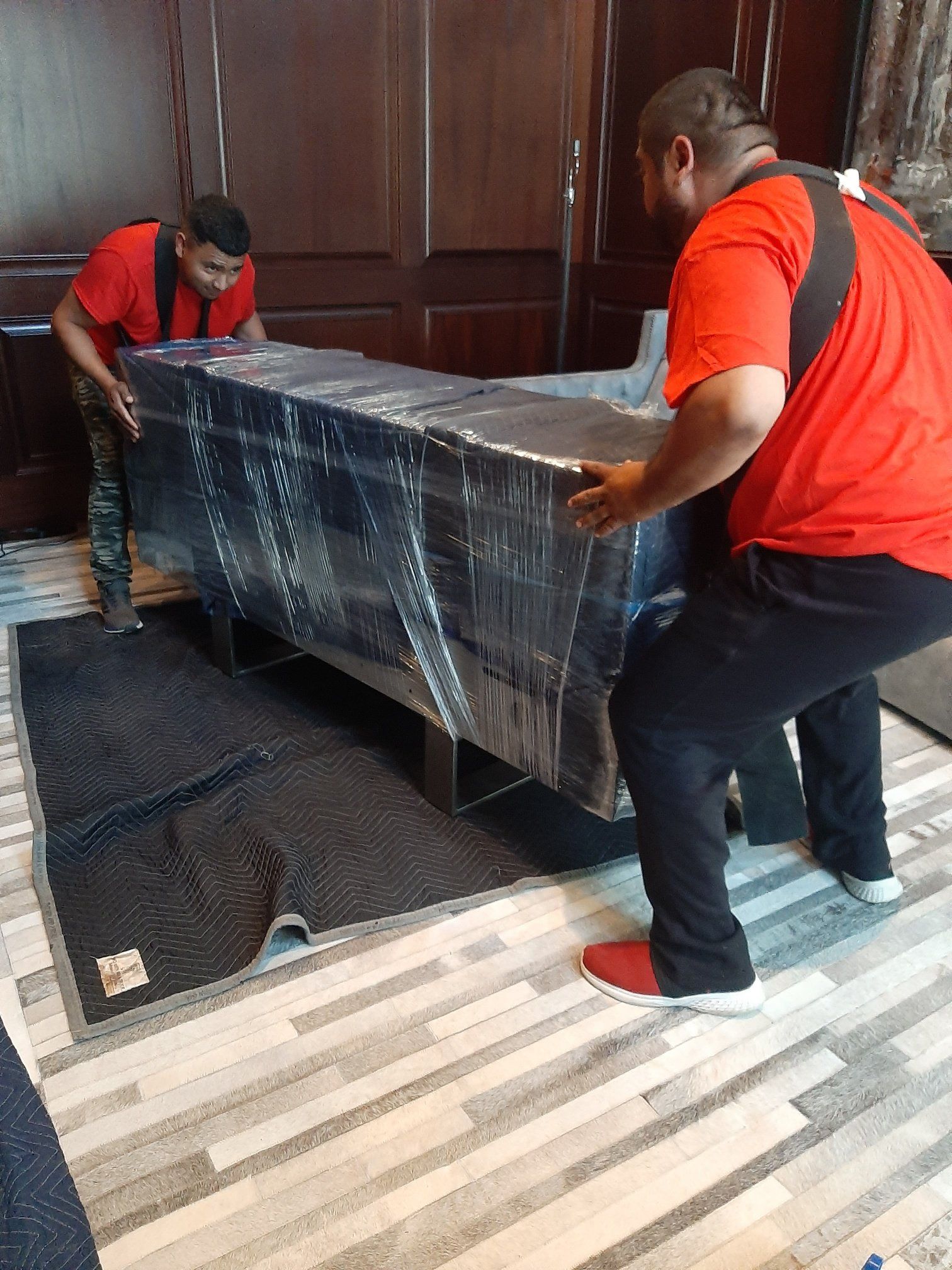 Two men are carrying a couch wrapped in plastic.