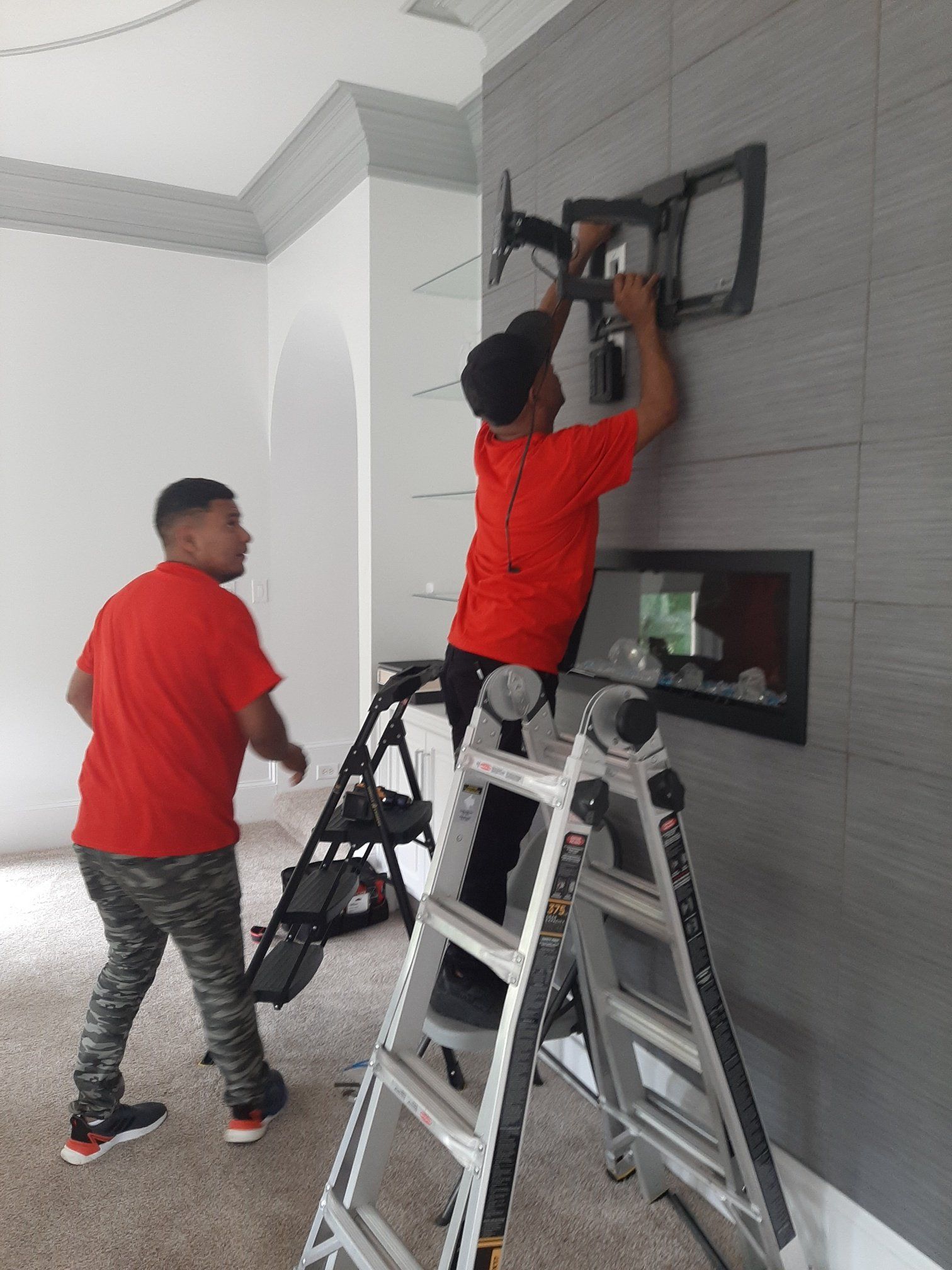 Two men are working on a tv mount on a wall.